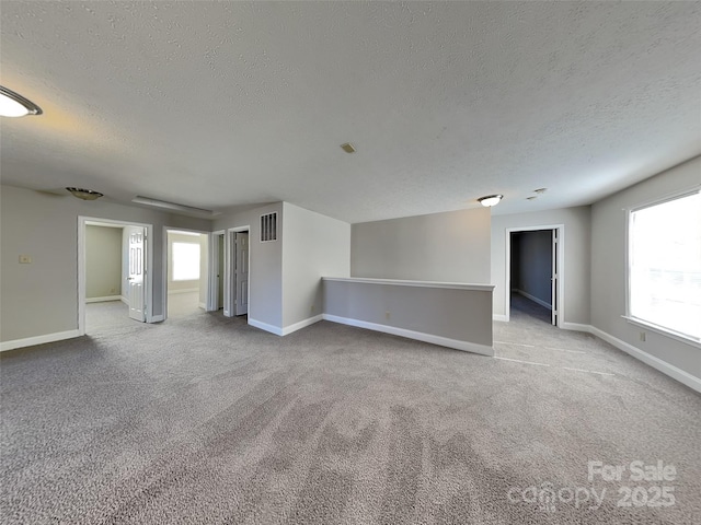 spare room with a textured ceiling, carpet, visible vents, and baseboards