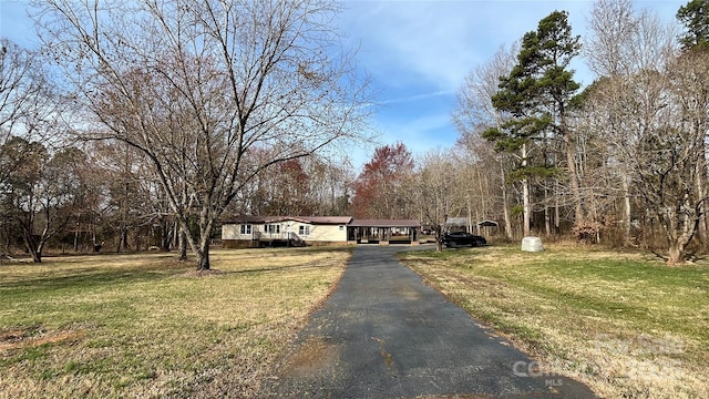 manufactured / mobile home with aphalt driveway, a carport, and a front lawn