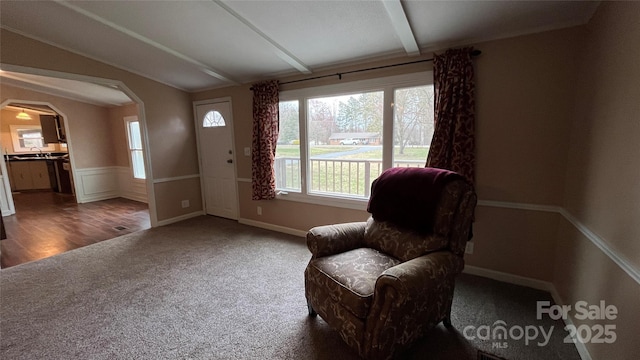 sitting room with arched walkways, wainscoting, lofted ceiling with beams, and carpet