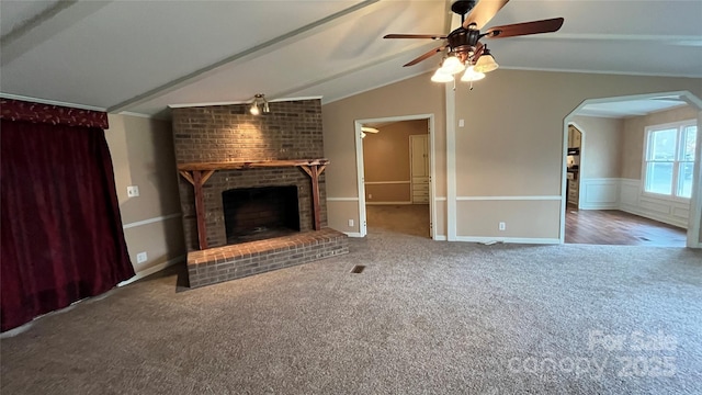 unfurnished living room featuring carpet, lofted ceiling, wainscoting, a fireplace, and arched walkways