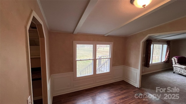 unfurnished room with a wainscoted wall, dark wood-type flooring, lofted ceiling with beams, and arched walkways