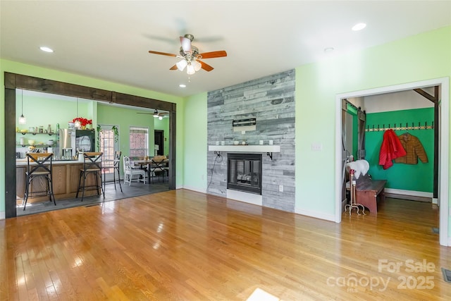 living room featuring wood finished floors, a ceiling fan, baseboards, recessed lighting, and a stone fireplace