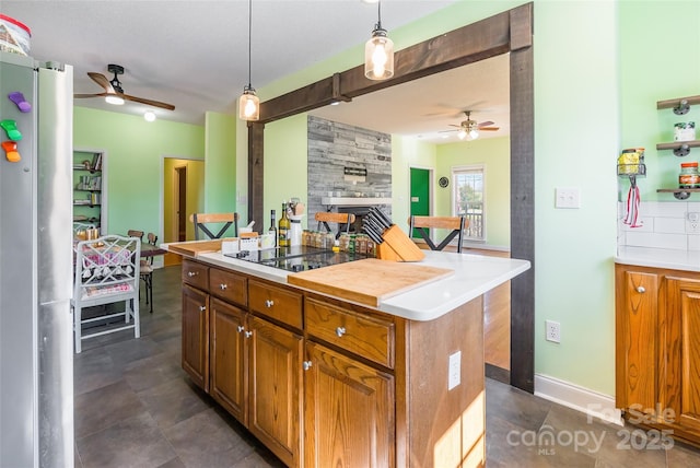 kitchen featuring black electric cooktop, ceiling fan, a fireplace, and freestanding refrigerator