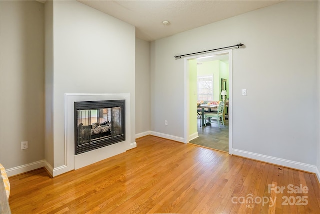 unfurnished living room with light wood-style flooring, baseboards, and a multi sided fireplace