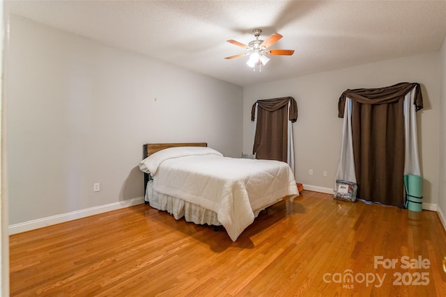 bedroom with light wood-type flooring, baseboards, a textured ceiling, and ceiling fan