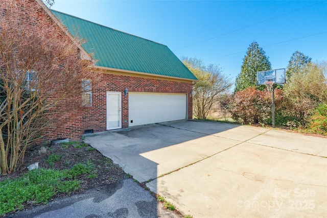 view of property exterior with metal roof, brick siding, an attached garage, and driveway