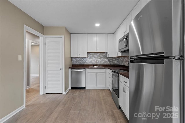 kitchen with light wood-style flooring, a sink, white cabinetry, stainless steel appliances, and wooden counters