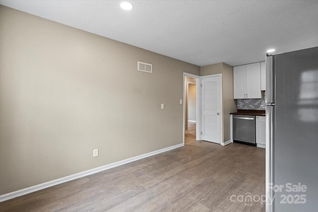 kitchen featuring wood finished floors, visible vents, stainless steel appliances, decorative backsplash, and white cabinets