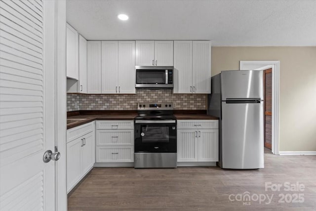 kitchen with decorative backsplash, white cabinets, wood finished floors, and appliances with stainless steel finishes