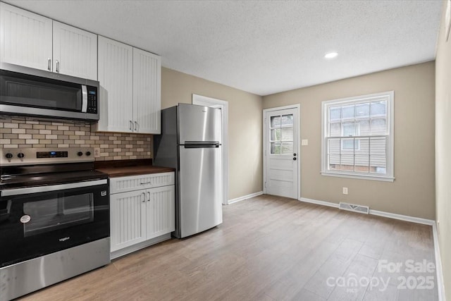 kitchen featuring visible vents, light wood-style flooring, tasteful backsplash, stainless steel appliances, and white cabinets