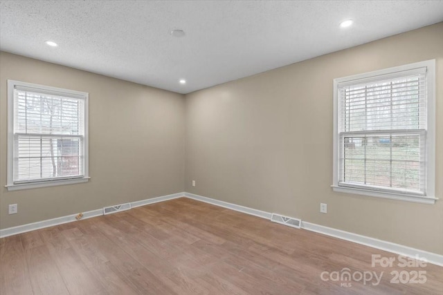 empty room featuring a textured ceiling, wood finished floors, visible vents, and baseboards