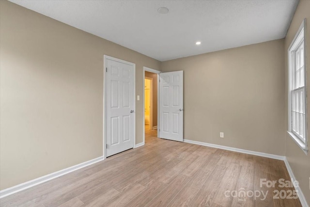 unfurnished bedroom with recessed lighting, multiple windows, baseboards, and wood finished floors