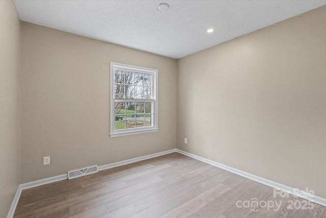 spare room featuring visible vents, baseboards, a textured ceiling, and wood finished floors