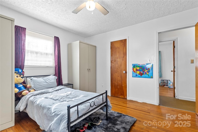 bedroom featuring a ceiling fan, light wood-style floors, baseboards, and a textured ceiling