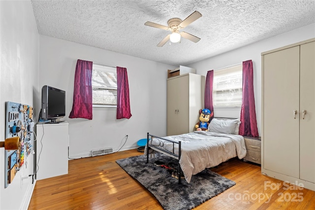 bedroom featuring multiple windows, a textured ceiling, a ceiling fan, and hardwood / wood-style flooring