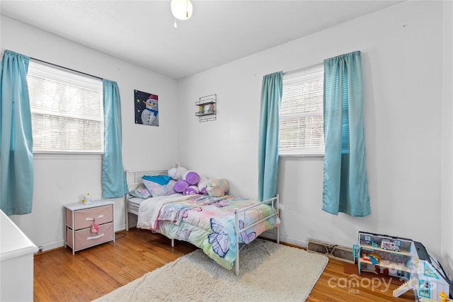 bedroom with multiple windows, wood finished floors, visible vents, and baseboards