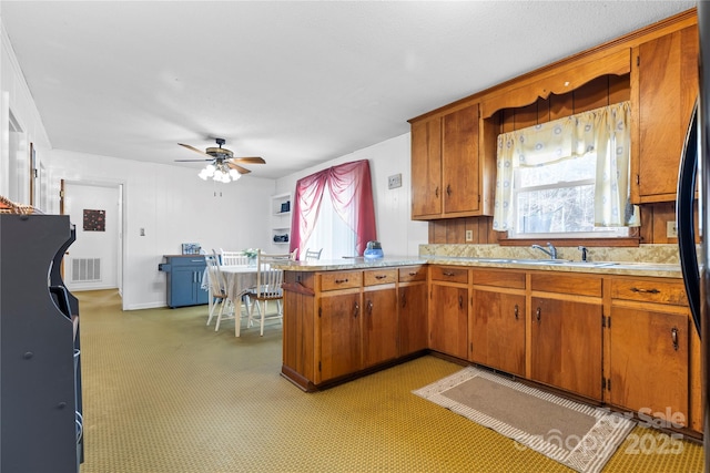 kitchen with brown cabinetry, visible vents, a peninsula, a sink, and light countertops