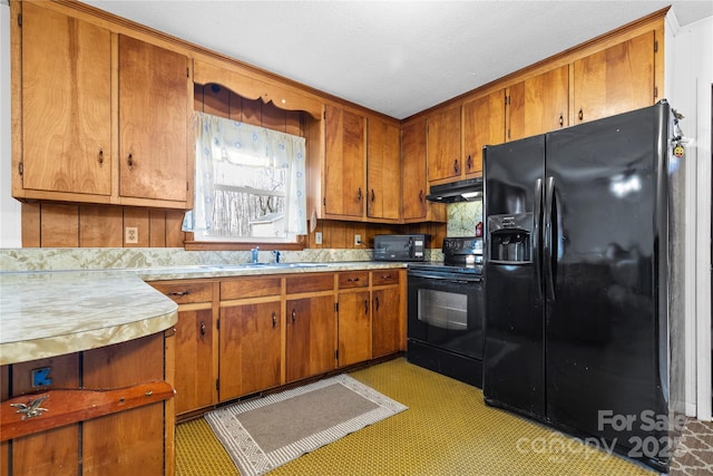 kitchen featuring under cabinet range hood, light countertops, brown cabinets, black appliances, and a sink