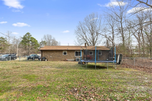 rear view of house with a fenced backyard, a chimney, a trampoline, a lawn, and brick siding