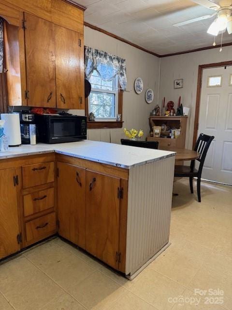 kitchen with brown cabinetry, a peninsula, ornamental molding, light countertops, and black microwave