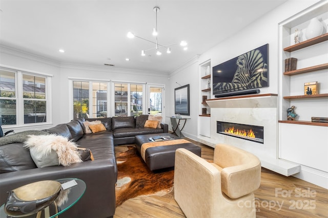 living room with a high end fireplace, built in features, ornamental molding, and wood finished floors