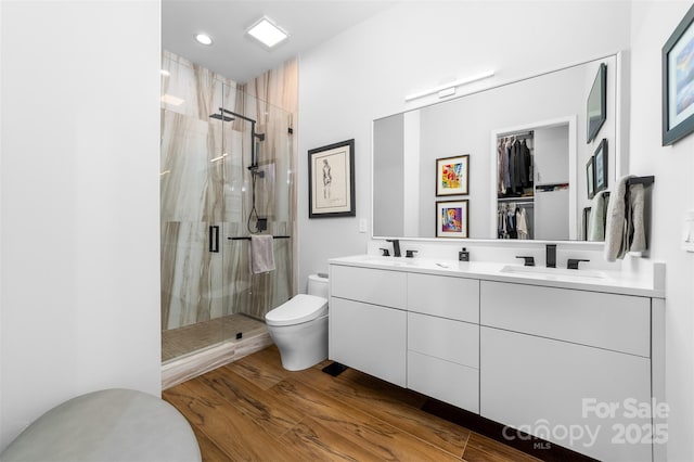 bathroom with a shower stall, toilet, wood finished floors, and a sink