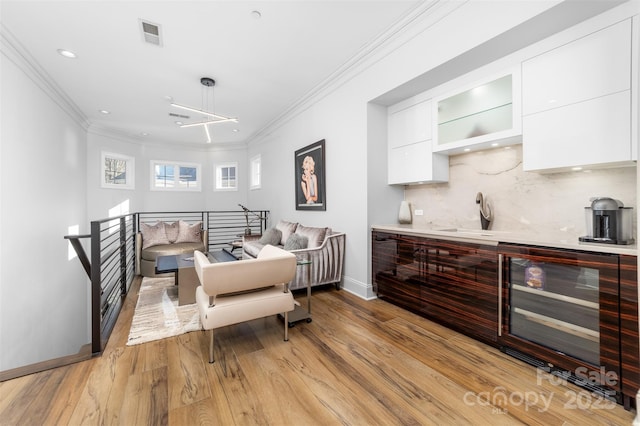 dining space featuring visible vents, baseboards, light wood-style flooring, wine cooler, and crown molding