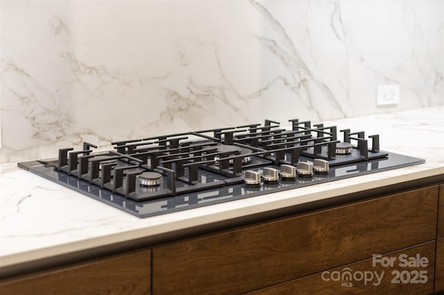 interior details with decorative backsplash, light countertops, and black gas stovetop