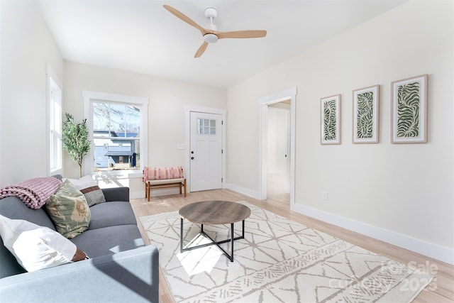 living room featuring light wood-type flooring, baseboards, and a ceiling fan