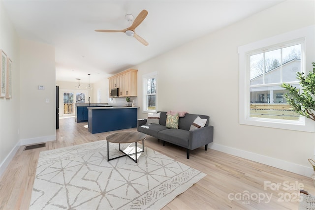 living room featuring light wood finished floors, visible vents, ceiling fan, and baseboards