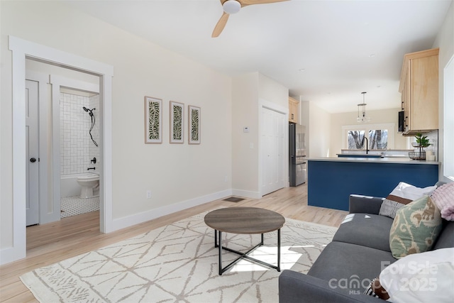 living area with light wood-style floors, baseboards, and ceiling fan