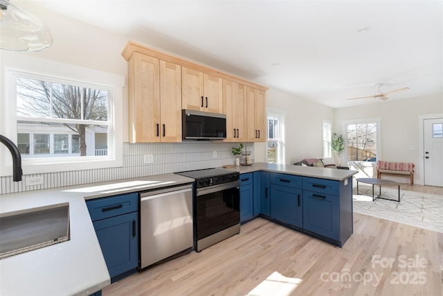 kitchen with light brown cabinets, stainless steel appliances, light wood-style floors, and a peninsula