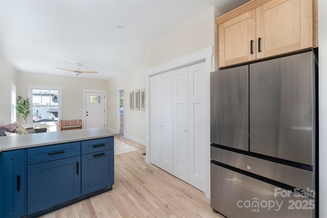 kitchen featuring blue cabinets, light wood-style flooring, light brown cabinets, freestanding refrigerator, and light countertops