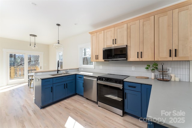 kitchen with light brown cabinets, a peninsula, a sink, light countertops, and appliances with stainless steel finishes