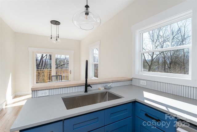 kitchen with blue cabinets, a sink, decorative light fixtures, light wood finished floors, and light countertops