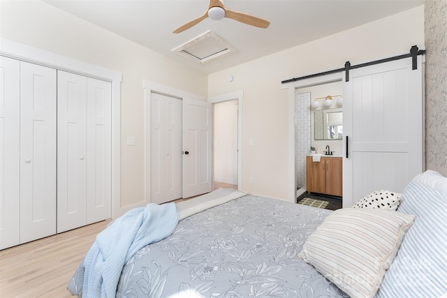 bedroom featuring a barn door, wood finished floors, ensuite bath, a ceiling fan, and a sink