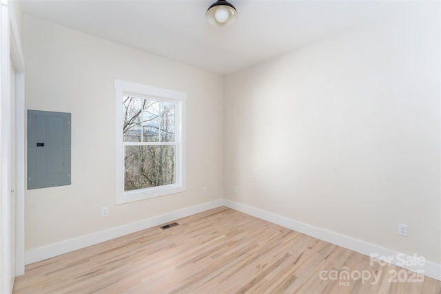 unfurnished room featuring electric panel, visible vents, baseboards, and wood finished floors