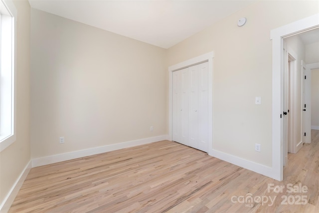 unfurnished bedroom with a closet, baseboards, and light wood-style floors