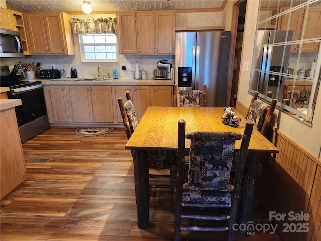 kitchen with a wainscoted wall, a sink, open shelves, dark wood-style floors, and stainless steel appliances