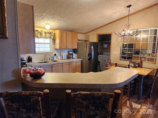 kitchen featuring a sink, washer and dryer, stainless steel appliances, an inviting chandelier, and lofted ceiling