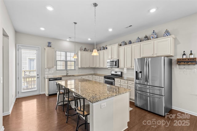 kitchen featuring visible vents, a kitchen island, stainless steel appliances, dark wood-type flooring, and backsplash