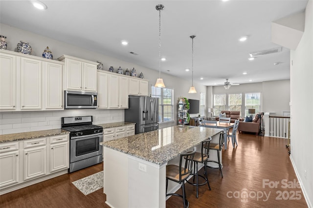 kitchen with visible vents, a kitchen island, dark wood-type flooring, appliances with stainless steel finishes, and backsplash