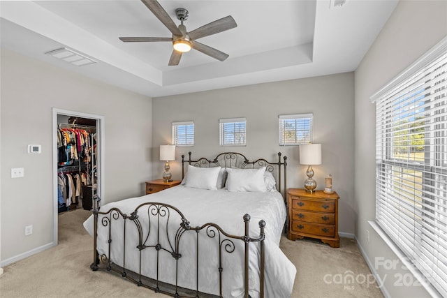 bedroom with multiple windows, a raised ceiling, light colored carpet, and a spacious closet