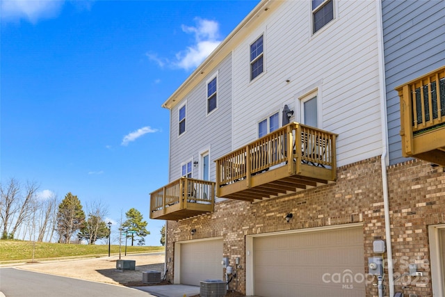 back of property with central air condition unit, a garage, brick siding, and driveway