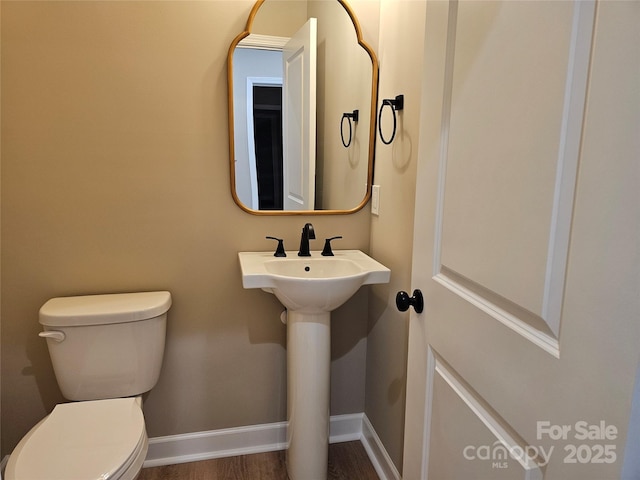 half bathroom with a sink, baseboards, toilet, and wood finished floors