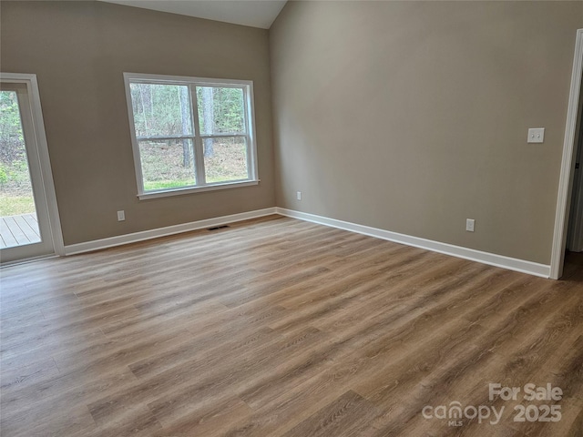 unfurnished room featuring a wealth of natural light, visible vents, baseboards, and wood finished floors