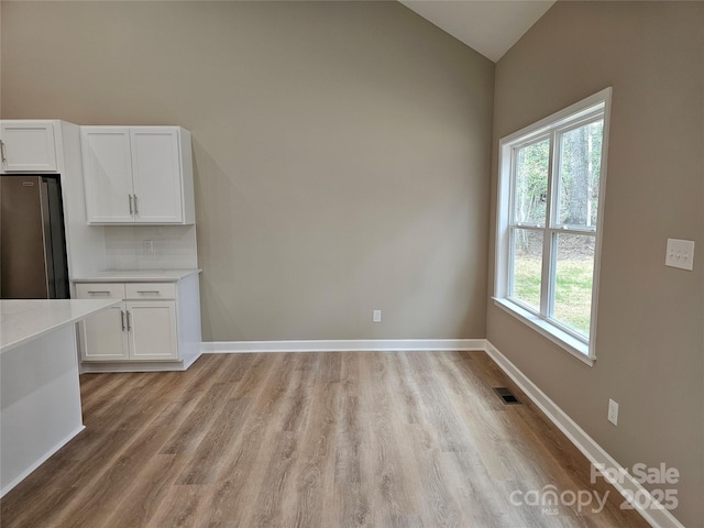 unfurnished dining area with lofted ceiling, light wood-style flooring, baseboards, and visible vents