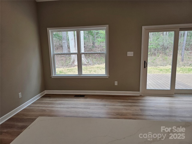 unfurnished room featuring wood finished floors, visible vents, and baseboards