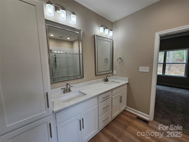 full bath featuring double vanity, visible vents, a shower with shower door, and a sink