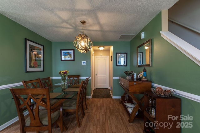 dining area with a notable chandelier, wood finished floors, baseboards, and a textured ceiling